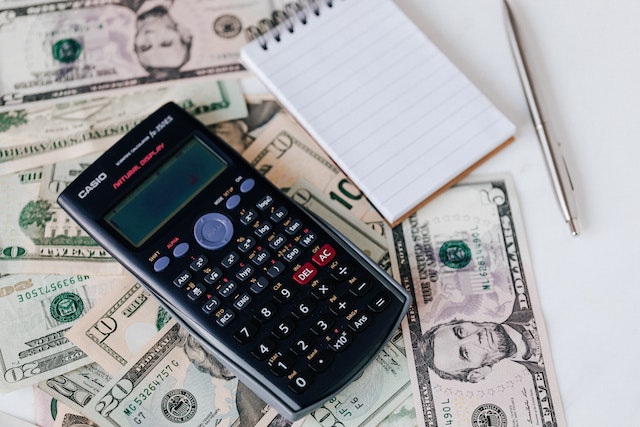 Black calculator beside a lined notebook and on top of U.S. dollars